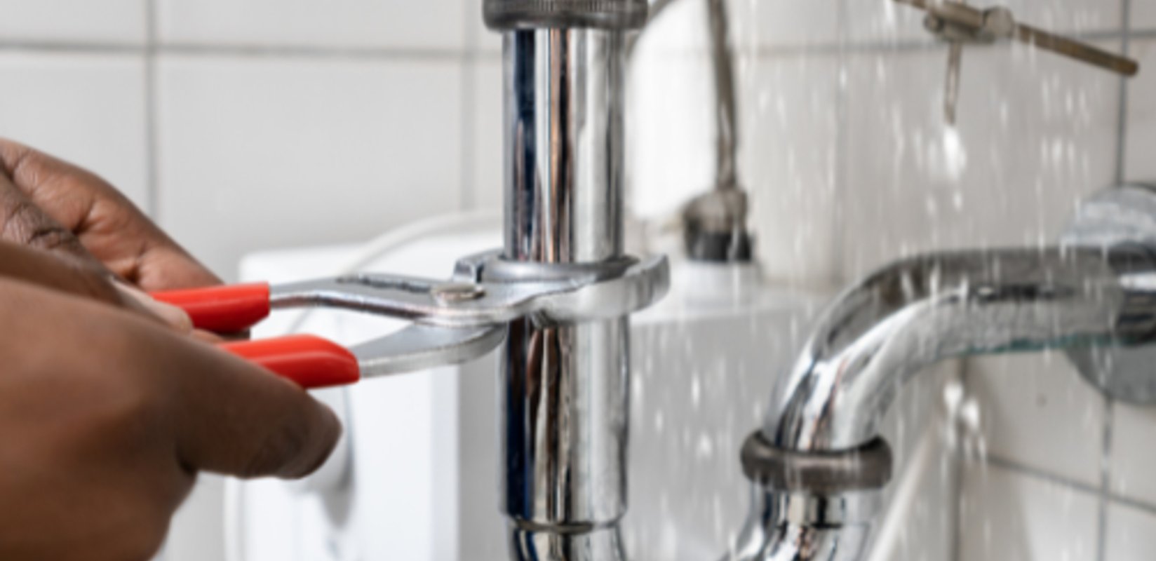 Plumber working on a leaking pipe beneath a sink